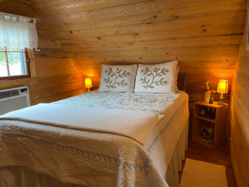 Cozy bedroom with a wooden interior, featuring a double bed, decorative pillows, and soft lighting.